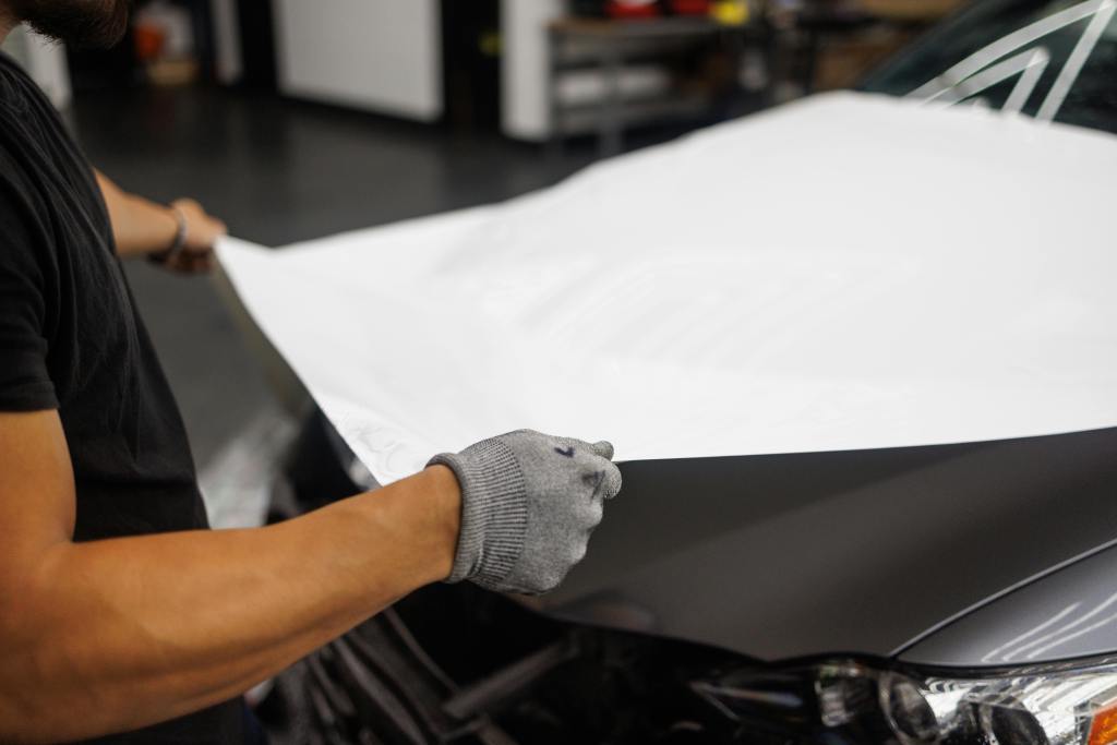 best ppf installation in Bangalore. Person applying vinyl wrap to car hood in garage setting.