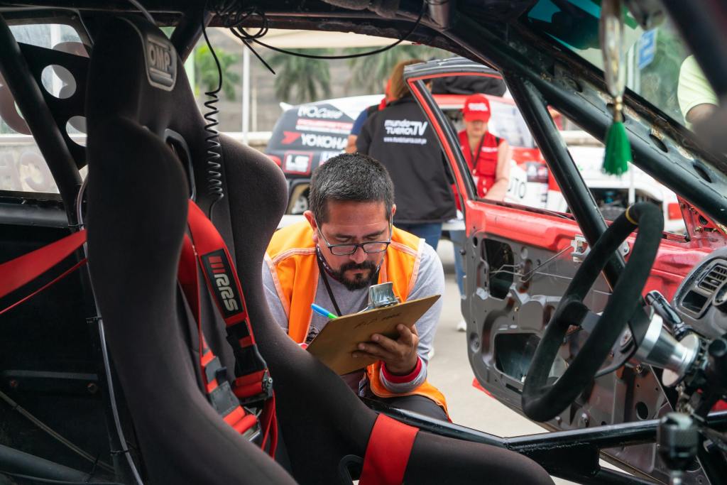 doorstep car service in Bangalore - BestFitment. A man inspects a race car interior at a motorsport event, noting findings on a clipboard.