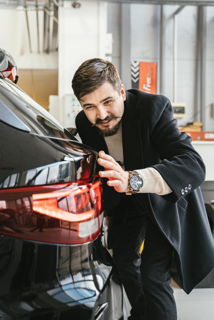 doorstep car service in Bangalore - BestFitment. Man in business attire examining a car in an indoor setting, suggesting car maintenance or purchase.